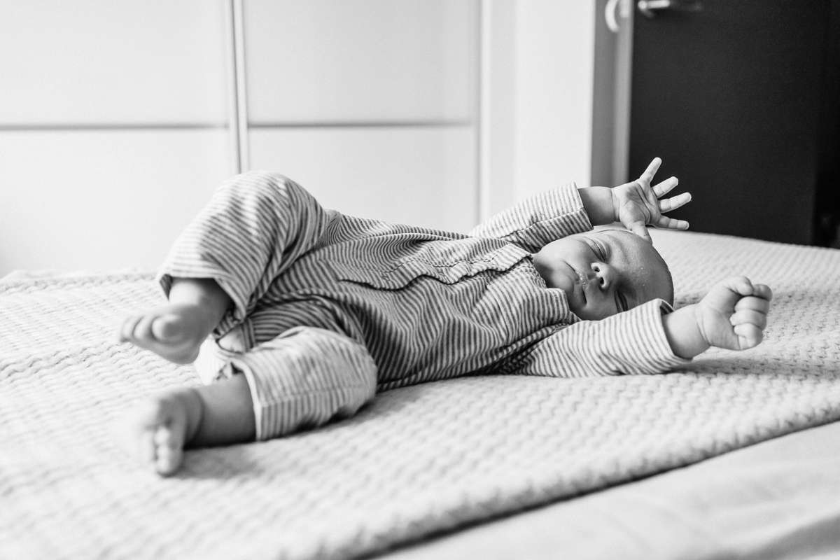 B&W image of newborn baby boy startling on parents bed, taken by Natalie Avery North London Newborn Photography.